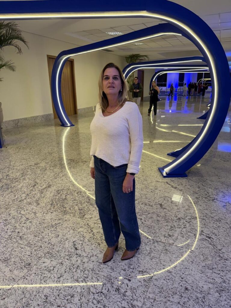 Gestora da Escola Jeitinho de Criança posando em um corredor iluminado durante o Fórum de Mantenedores da SAS Educação