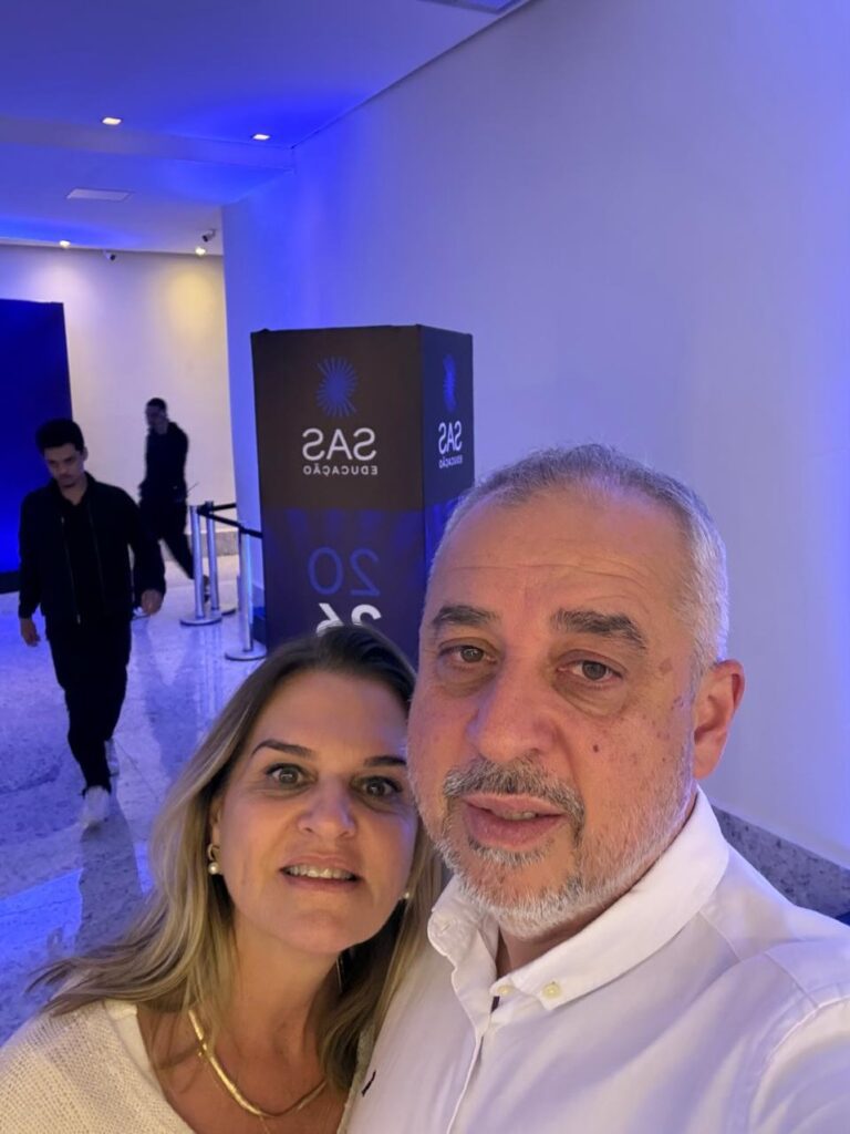 Gestora e mantenedora da Escola Jeitinho de Criança em selfie com um colega ao lado de um totem da SAS Educação