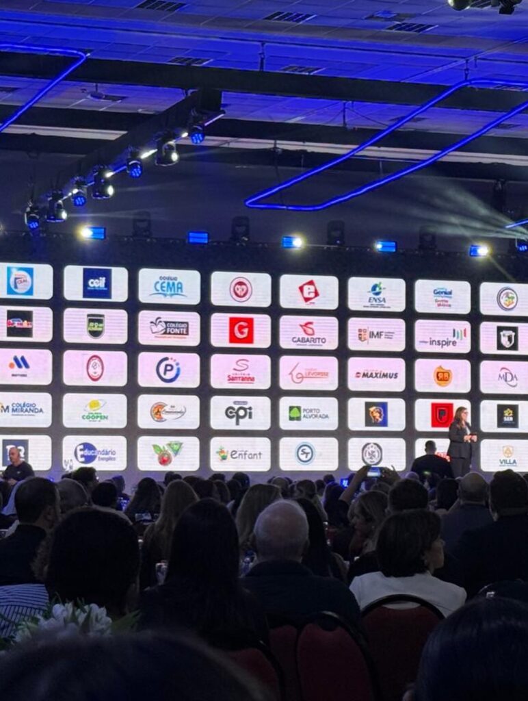Palco do Fórum de Mantenedores da SAS Educação com painel de logotipos de escolas parceiras e plateia